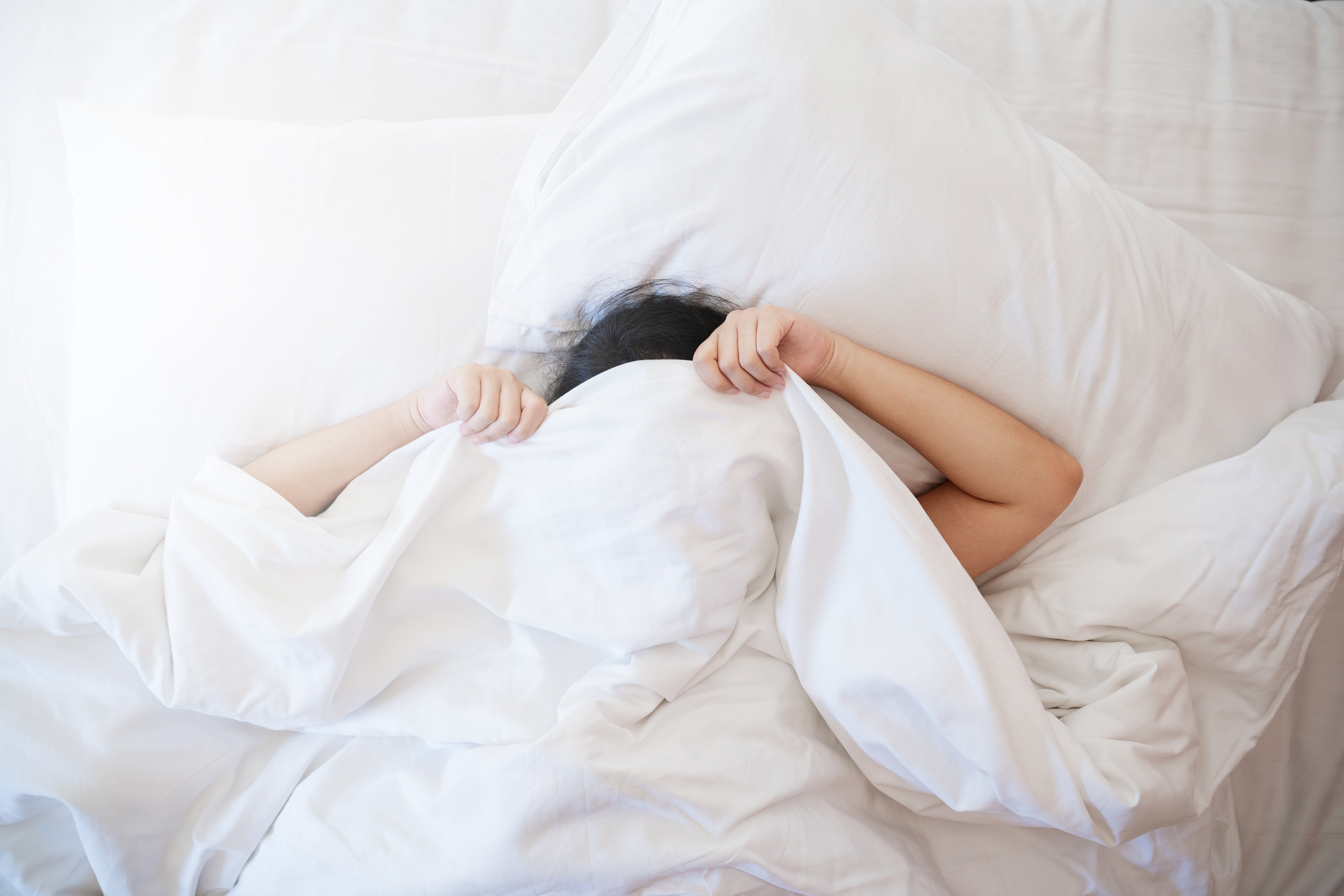 Woman relaxing on AnAká luxury organic cotton bedsheet, feeling its soft texture in a cozy bedroom